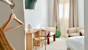 Een hotelkamer met een bed, twee stoelen, een tafel, een televisie en een grote vaas.