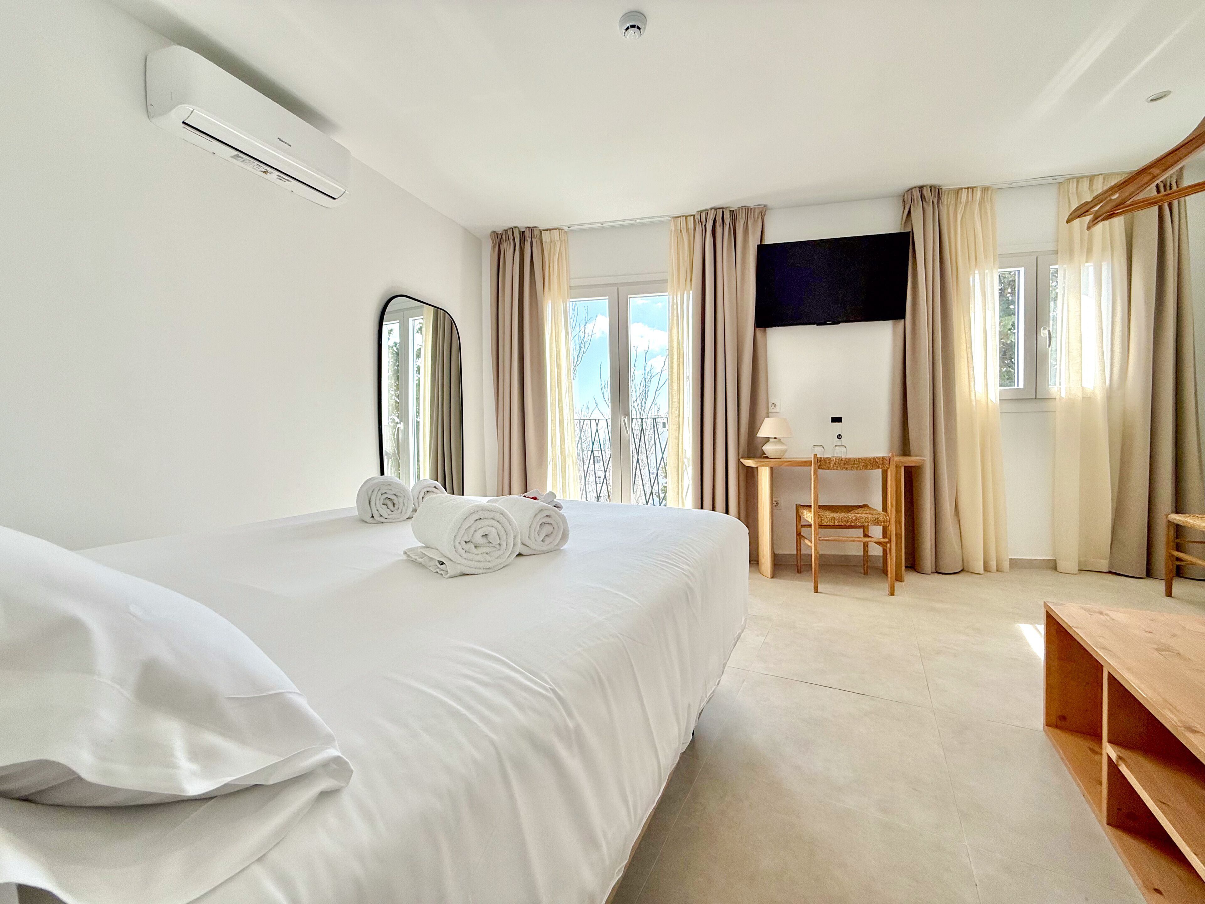 Een hotelkamer met een bed, bureau, stoel, televisie en een raam met gordijnen.