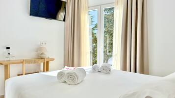 Habitación de hotel con cama, televisor montado en la pared, escritorio con lámpara y ventana con cortinas.