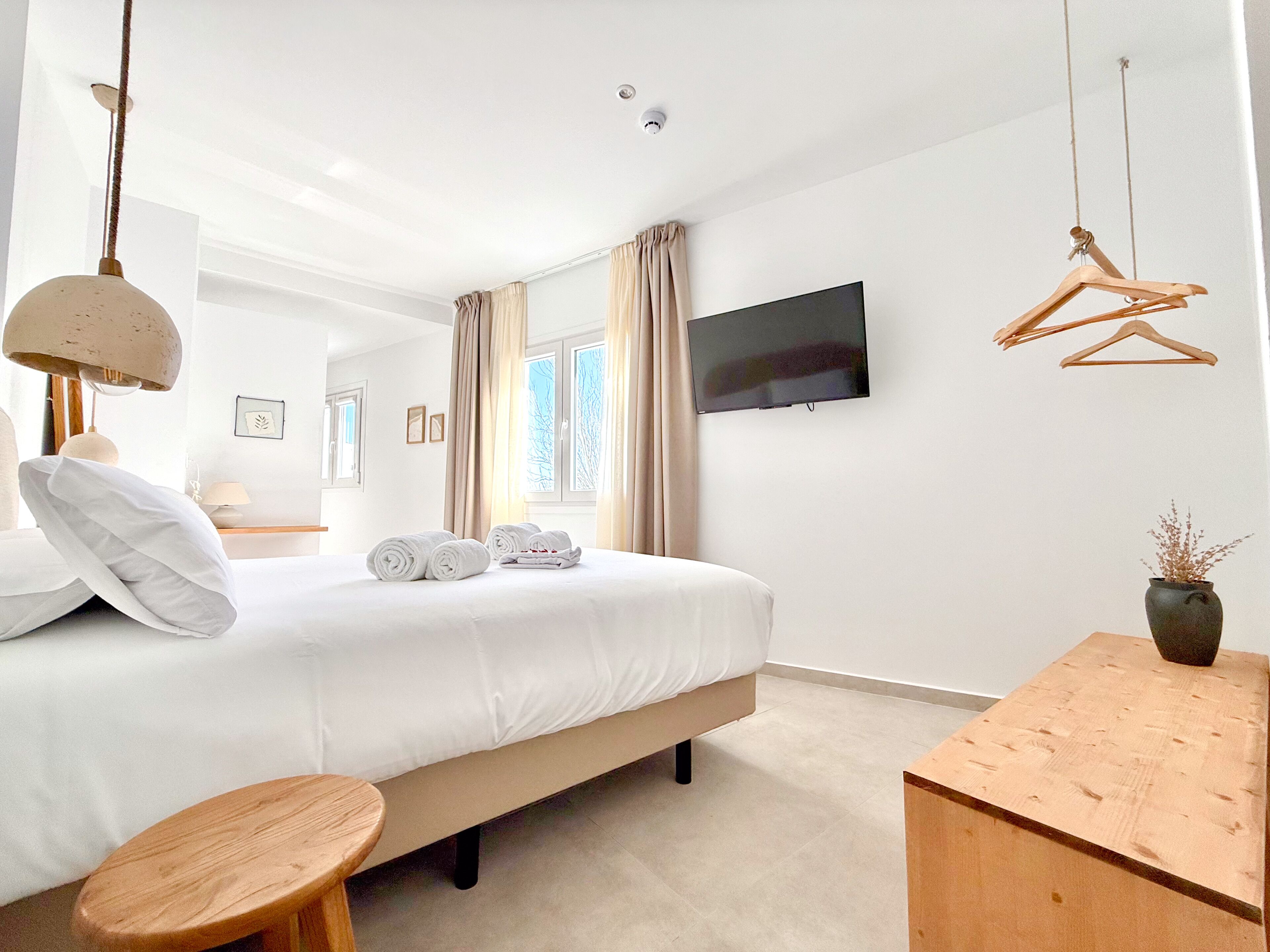 Un dormitorio con cama, televisor, mesa de madera y lámpara colgante.