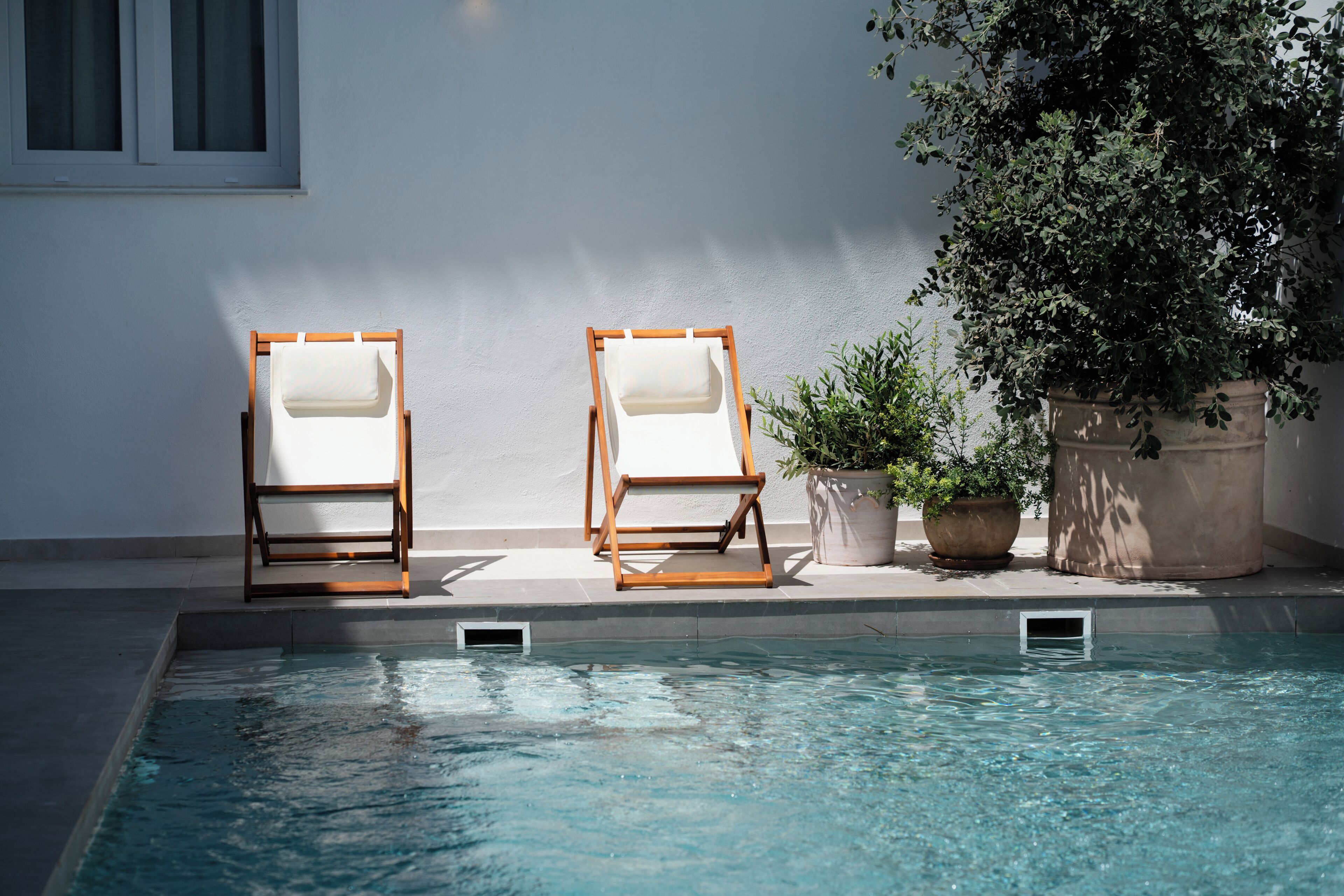 A poolside area with two wooden lounge chairs and a potted plant.
