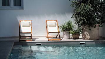 A poolside area with two wooden lounge chairs and a potted plant.