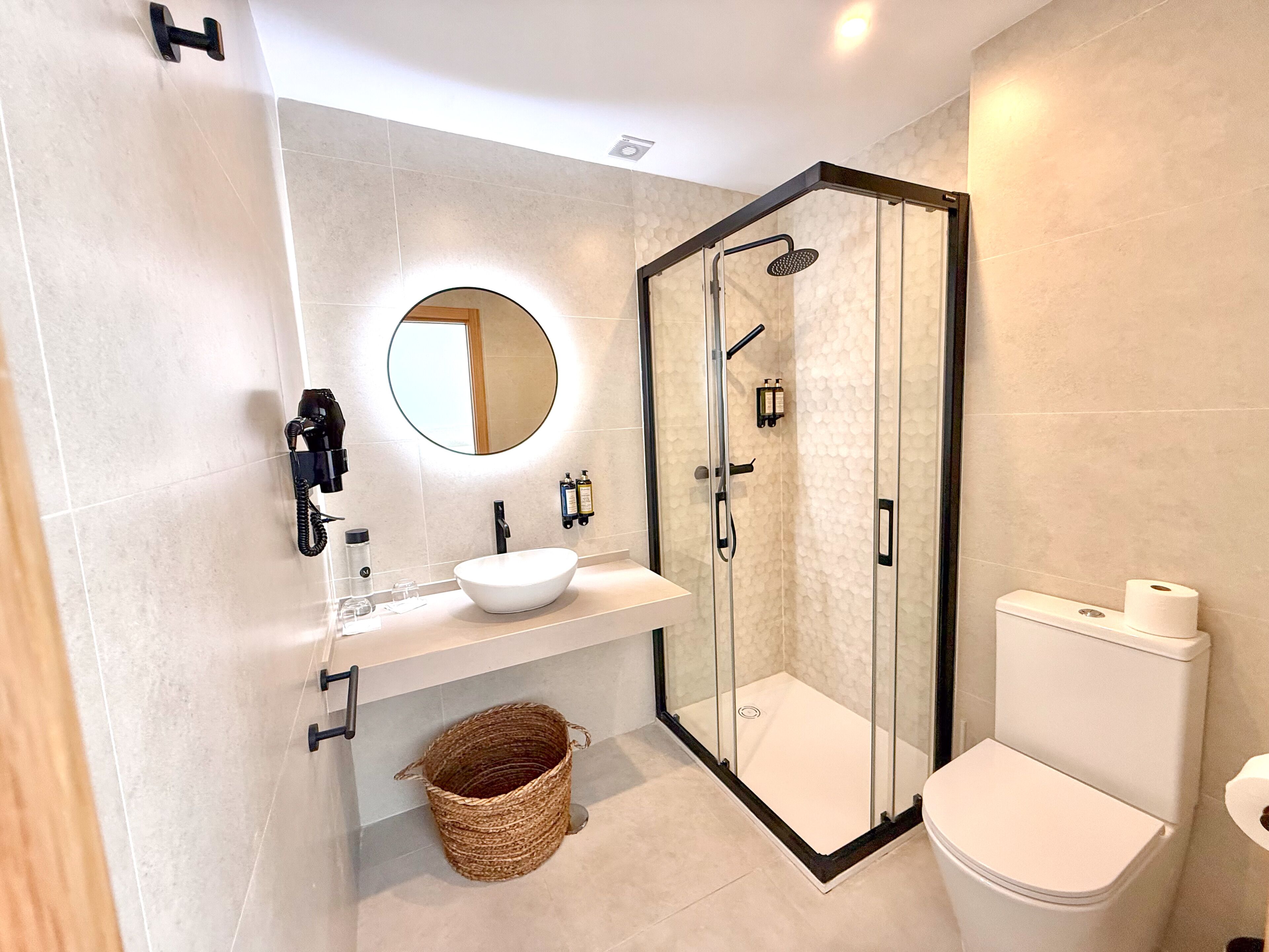 Een moderne badkamer met een douchecabine van glas, een ronde spiegel, een wit wastafelmeubel en een toilet.