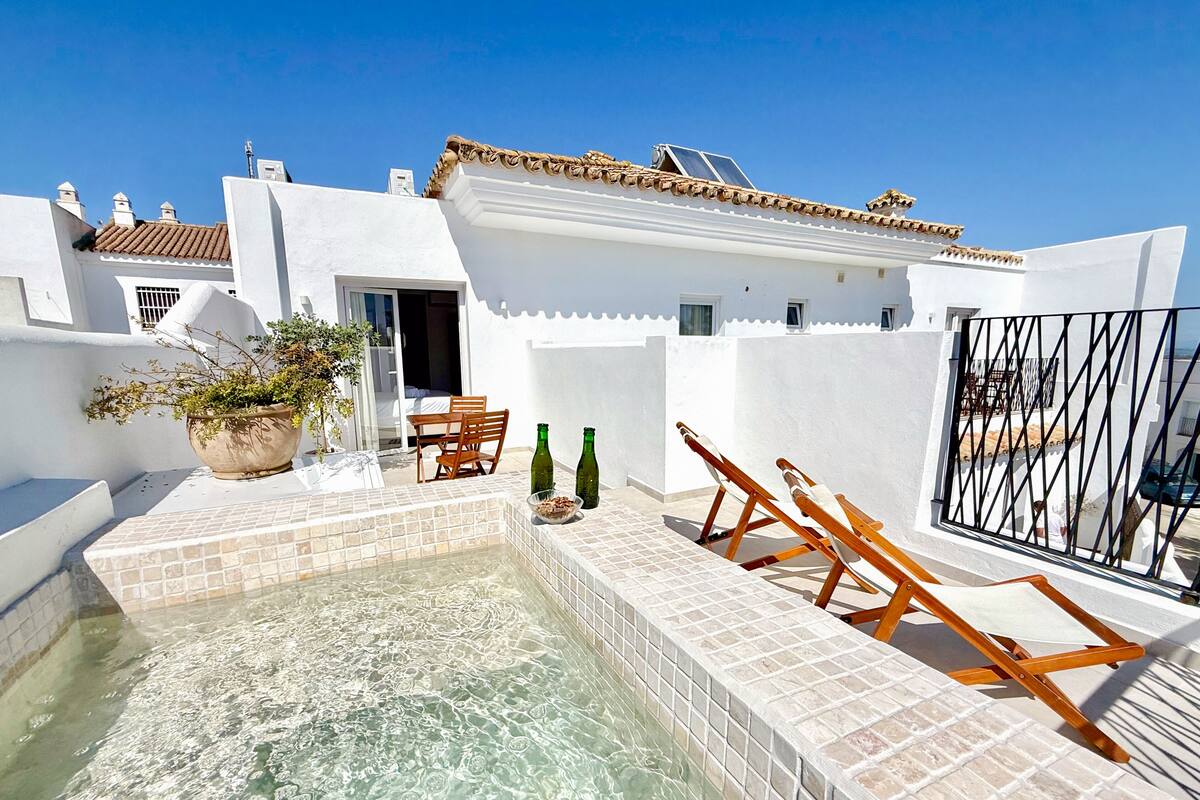 A rooftop pool with a tiled deck, a potted plant, and wooden lounge chairs.