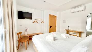 A hotel room with a bed, a desk, a chair, a TV, a door, and an air conditioning unit.