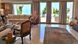 Un salon spacieux avec un grand canapé, une table basse et une vue sur la mer grâce à de grandes fenêtres.