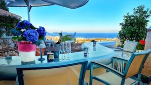 Un espace de restauration en plein air avec vue sur la mer, comprenant une table avec des chaises, un vase de fleurs et un verre de vin.