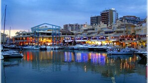 Un port de plaisance avec des bateaux amarrés, des bâtiments donnant sur le front de mer et une structure bleue imposante.