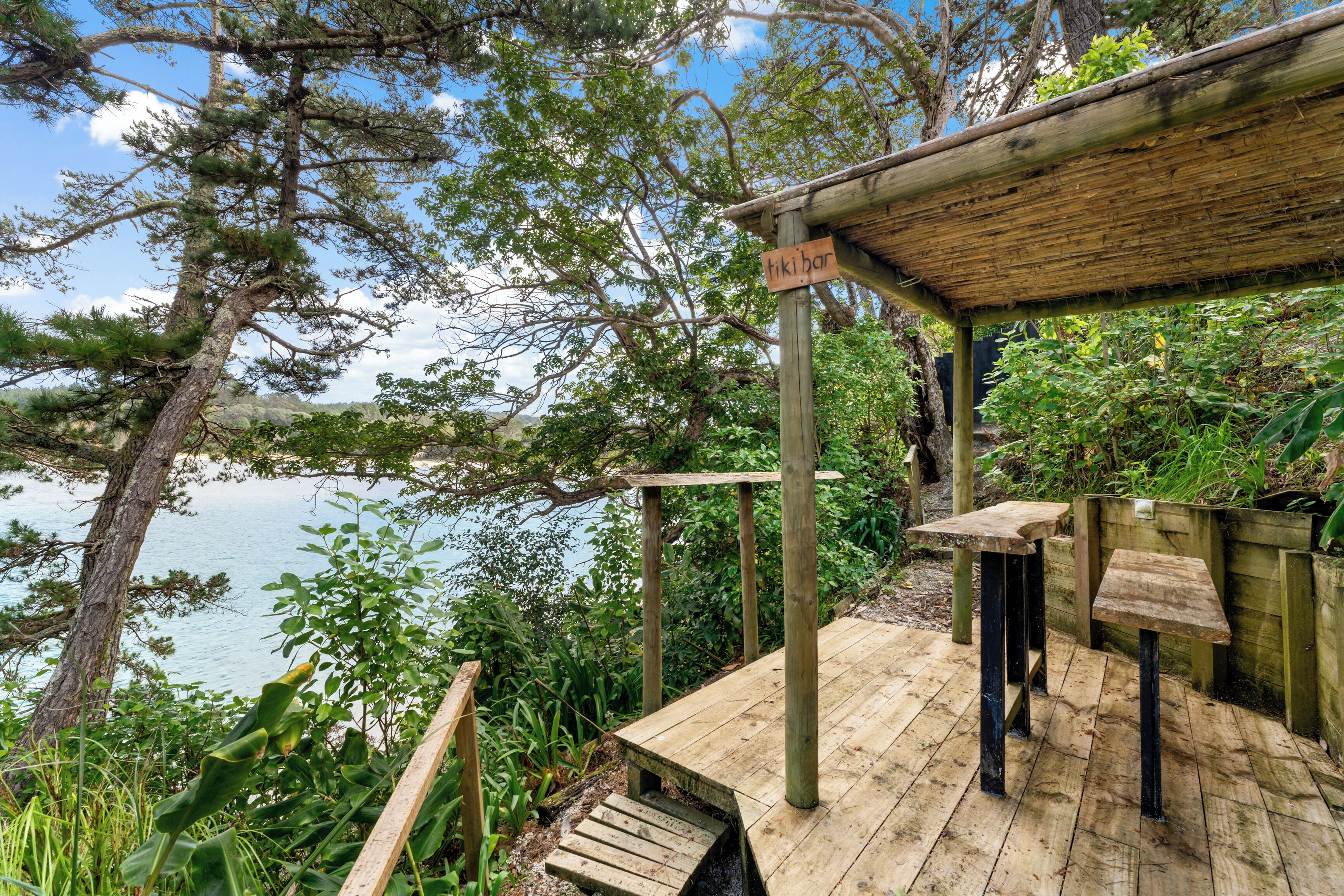 Um deck de madeira com pérgola, com vista para um corpo de água e rodeado por vegetação.