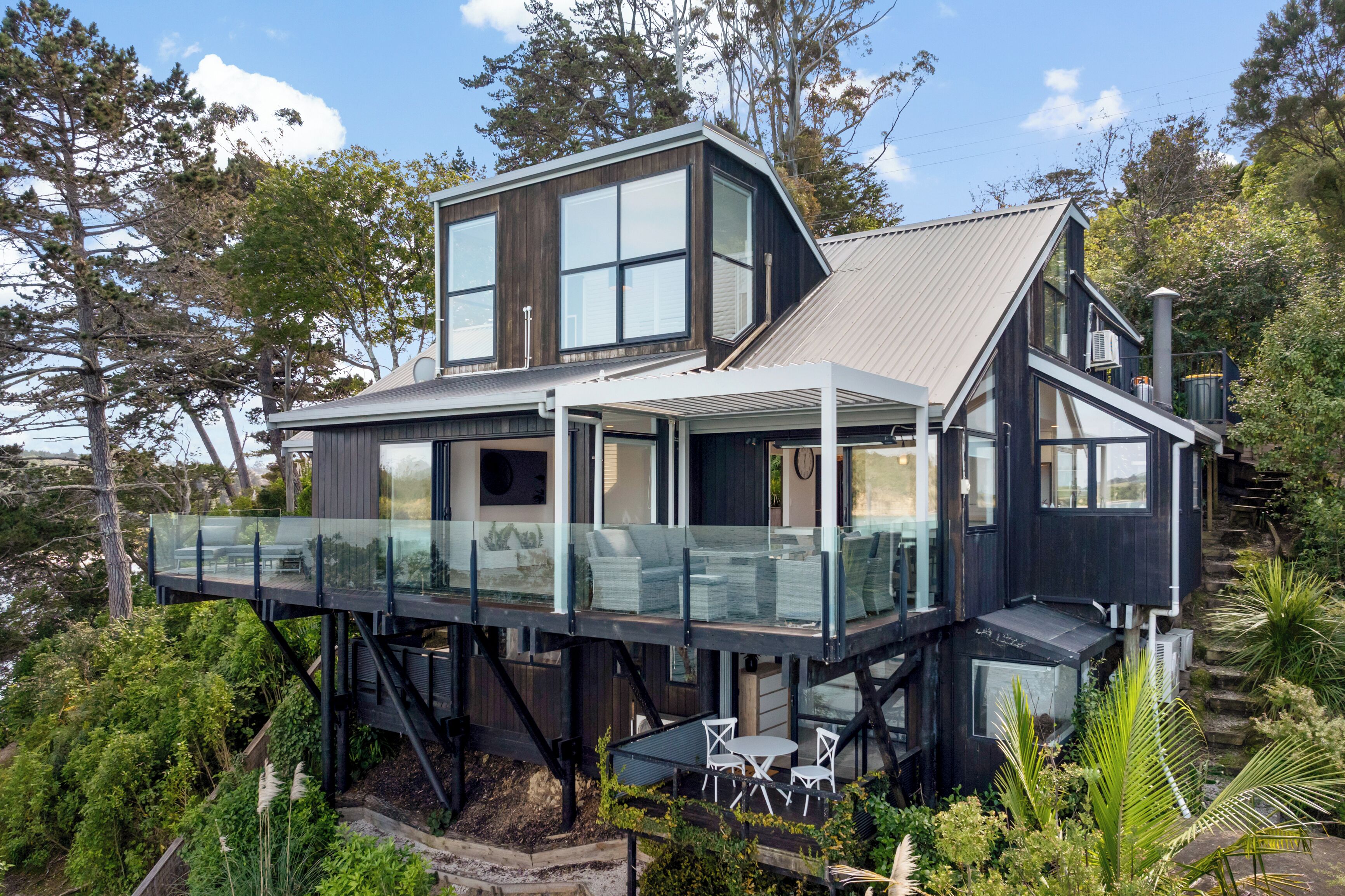 Une maison moderne dotée d’un balcon en verre, d’un deuxième étage et d’une grande fenêtre.