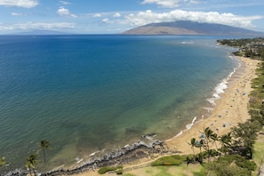 A beach with clear waters, a sandy shore, and a mountain in the background.