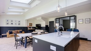Una cocina moderna con una isla central, comedor y sala de estar con sofá y televisor.