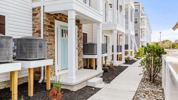 Une rangée d’immeubles résidentiels modernes à plusieurs étages, dotés de balcons, de climatiseurs extérieurs et d’un chemin bien entretenu.