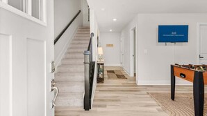 Un intérieur moderne avec un escalier, une table de baby-foot et un téléviseur à écran plat diffusant des images de « OCEANS EDGE VACATIONS ».