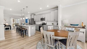 Une cuisine moderne avec des meubles blancs, un îlot central et un coin repas doté de chaises en bois.
