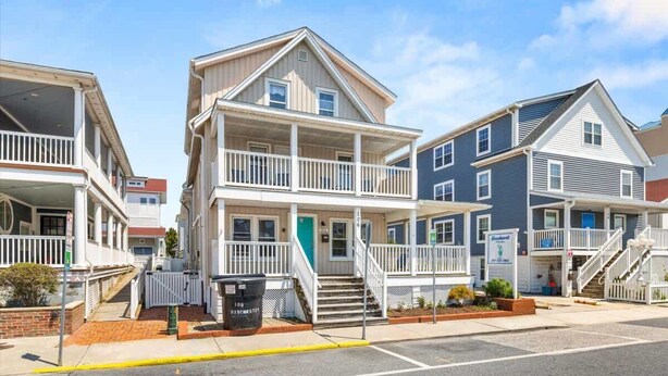 A row of multi-story residential buildings with balconies, a gated driveway, and a clear sky. - Dorchester Drift B: Shore Nest (Ocean City)