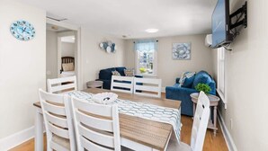A modern living room with a dining area, a blue sofa, and a flat-screen TV mounted on the wall. - Dorchester Drift B: Shore Nest (Ocean City)