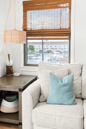 A living room with a sofa, a lamp, a window with blinds, and a view of a marina.