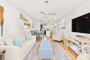 A living room with a sofa, ottoman, TV, and a dining area with chairs and a table.