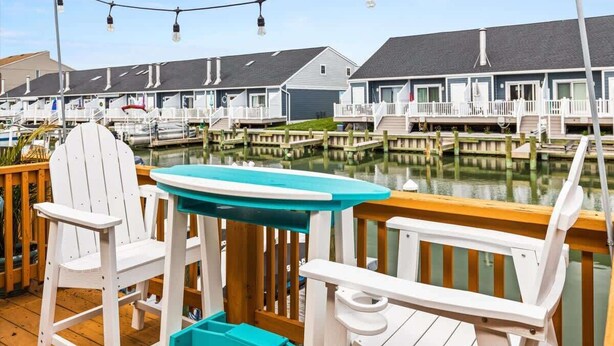 A waterfront property with wooden deck chairs, a small table, and string lights. - Blue Horizon at Old Port (Ocean City)