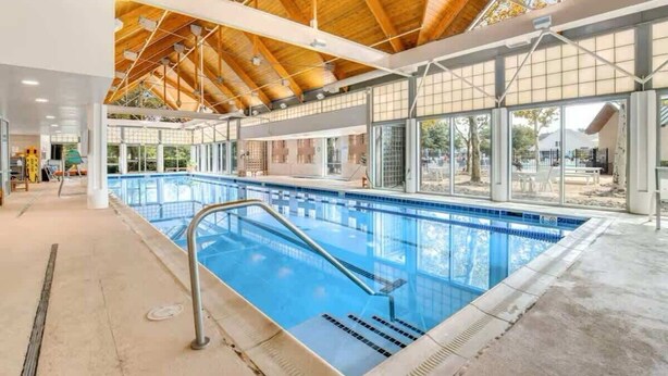 A large indoor swimming pool with a wooden ceiling and large windows.