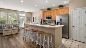A modern kitchen with a central island, wooden cabinets, stainless steel appliances, and a seating area with a sofa and bar stools.