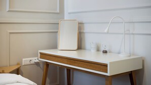 Et hvidt natbord med en trækuffe, en hvid lampe og et spejl.