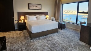 A modern hotel room with a large bed, a desk, a chair, and a view of the sea. - Hams Apartments (Duba)