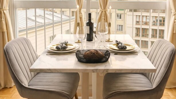 Une table à manger avec deux chaises, une bouteille, des verres et un panier de pain.