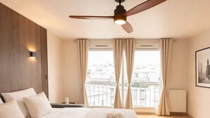 Une chambre d’hôtel avec un lit, un ventilateur de plafond, une fenêtre avec des rideaux et un radiateur.
