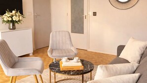 Un salon moderne avec un canapé gris, un fauteuil assorti, une table basse ronde sur laquelle repose un livre, et un miroir décoratif accroché au mur.