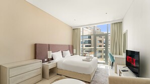 A modern hotel room with a large bed, a TV, a desk, and a view of the city. - Seven Palm - 1421 Studio (Dubai)