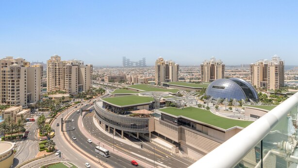 A high-rise building with a curved glass facade, surrounded by other tall buildings and a busy road with vehicles. - Seven Palm - 1421 Studio (Dubai)