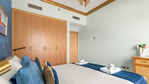 A hotel room with a large bed, wooden wardrobe, and a small desk with a vase of flowers. - Al Dabas - 707 2BD (Dubai)