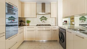 A modern kitchen with a built-in oven, microwave, and dishwasher, featuring a central island with a tree mural. - Al Dabas - 707 2BD (Dubai)