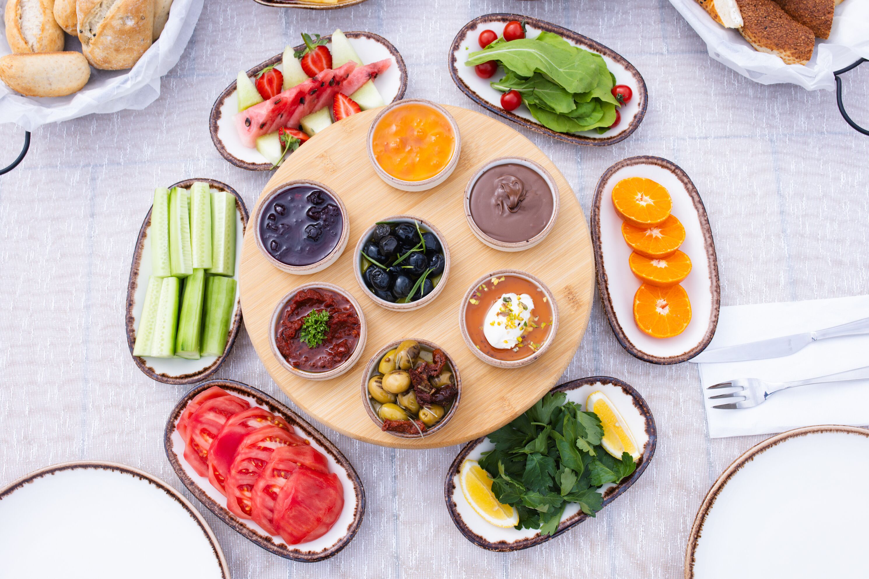 A variety of food items arranged on a wooden board, including sliced cucumbers, tomatoes, olives, and various dips.