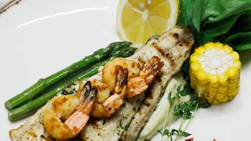 Un plato con pescado a la parrilla, camarones, espárragos, maíz y limón.
