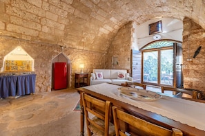 A rustic stone-walled room with a dining table set for two, a red refrigerator, and a white sofa. - Trullo Venneri in Alliste (Alliste)