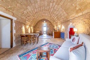 A rustic stone interior with a dining area, a sofa, and a patterned rug. - Trullo Venneri in Alliste (Alliste)