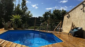 A wooden deck with a swimming pool, potted plants, and a barbecue area.