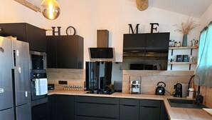 A modern kitchen with dark cabinetry, a wooden ceiling, and a hanging light fixture.