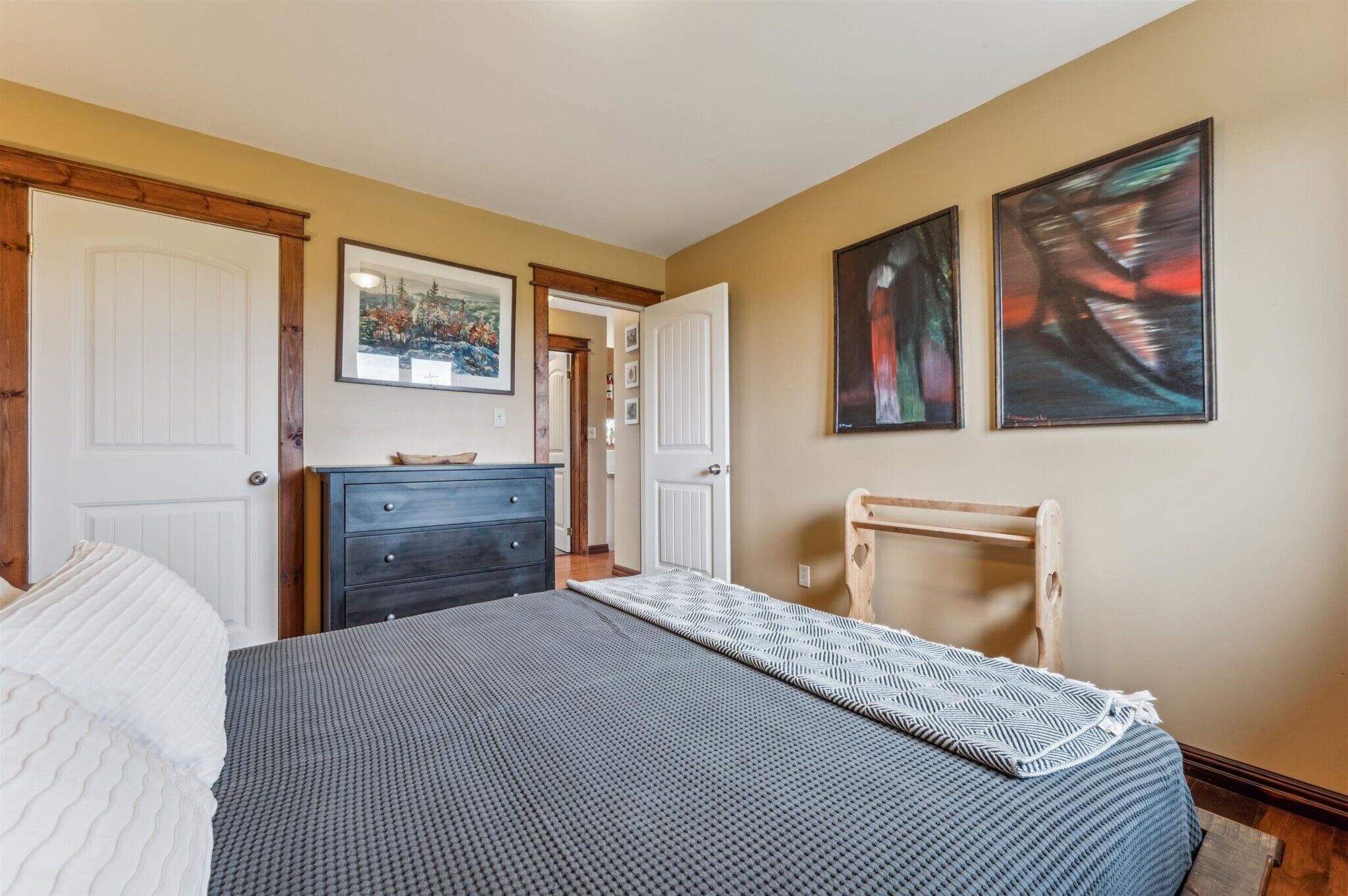 A bedroom with a bed, dresser, and two paintings on the wall.