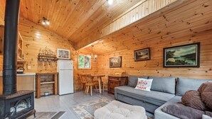 Un interior de cabaña acogedor con techo de madera, chimenea, sofá y comedor.