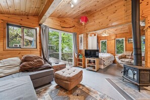 Ein gemütliches Blockhaus-Interieur mit Sofa, Hocker, Fernseher und Kaminofen.