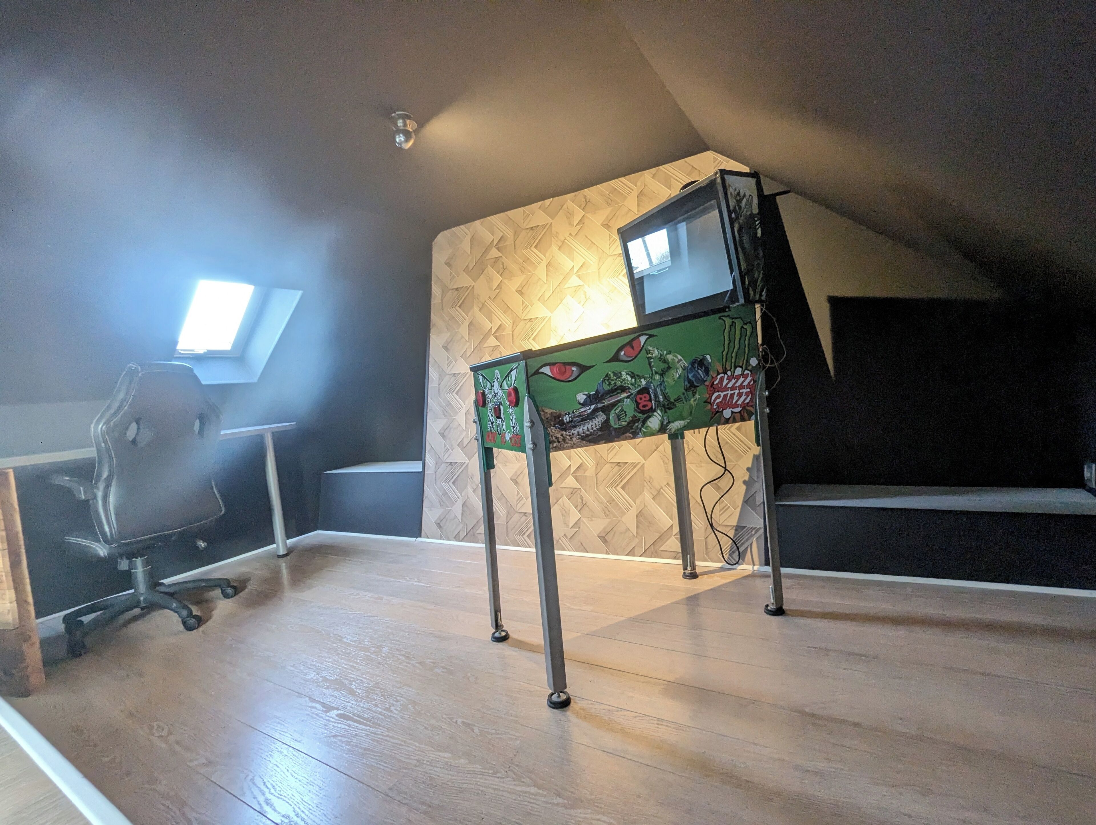 Une pièce comprenant un bureau, une chaise, une petite table ornée du logo de Monster Energy et un mur à motifs.