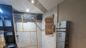 Ein modernes Badezimmer mit Dusche, einem Holzkosmetikschrank, einem schwarzen Waschbecken und einem Spiegel.
