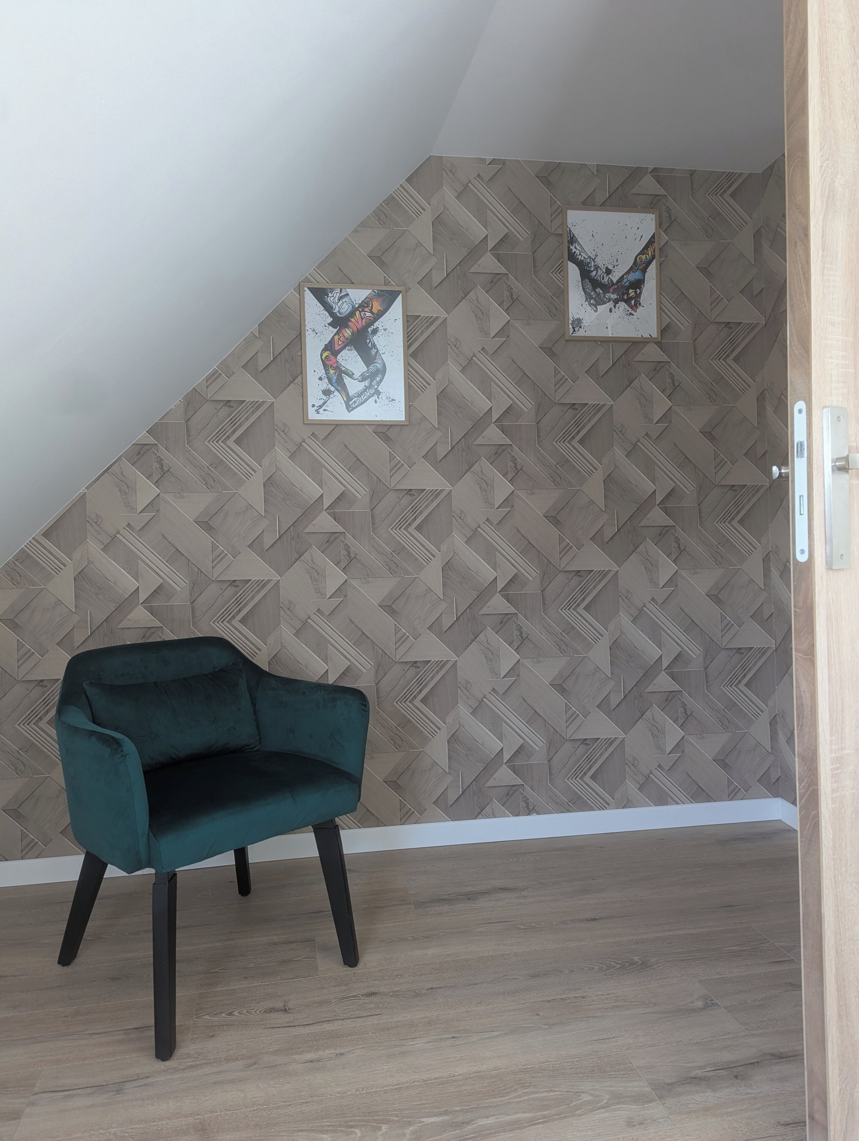 Una habitación con un revestimiento de pared con motivo de espiga, un sillón color turquesa y dos obras de arte enmarcadas.