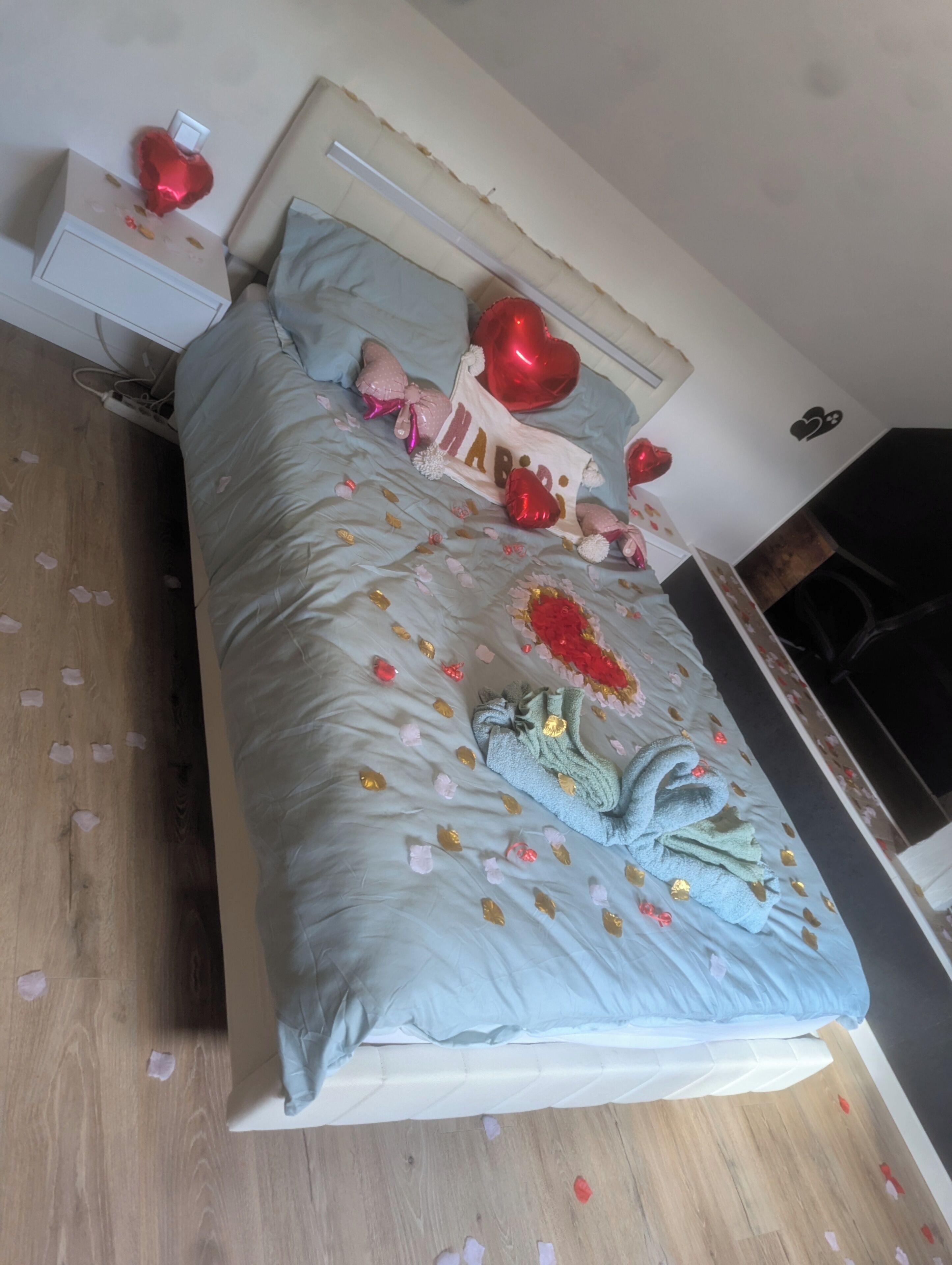 A bed with a light blue comforter, a decorative pillow, and a heart-shaped pillow.