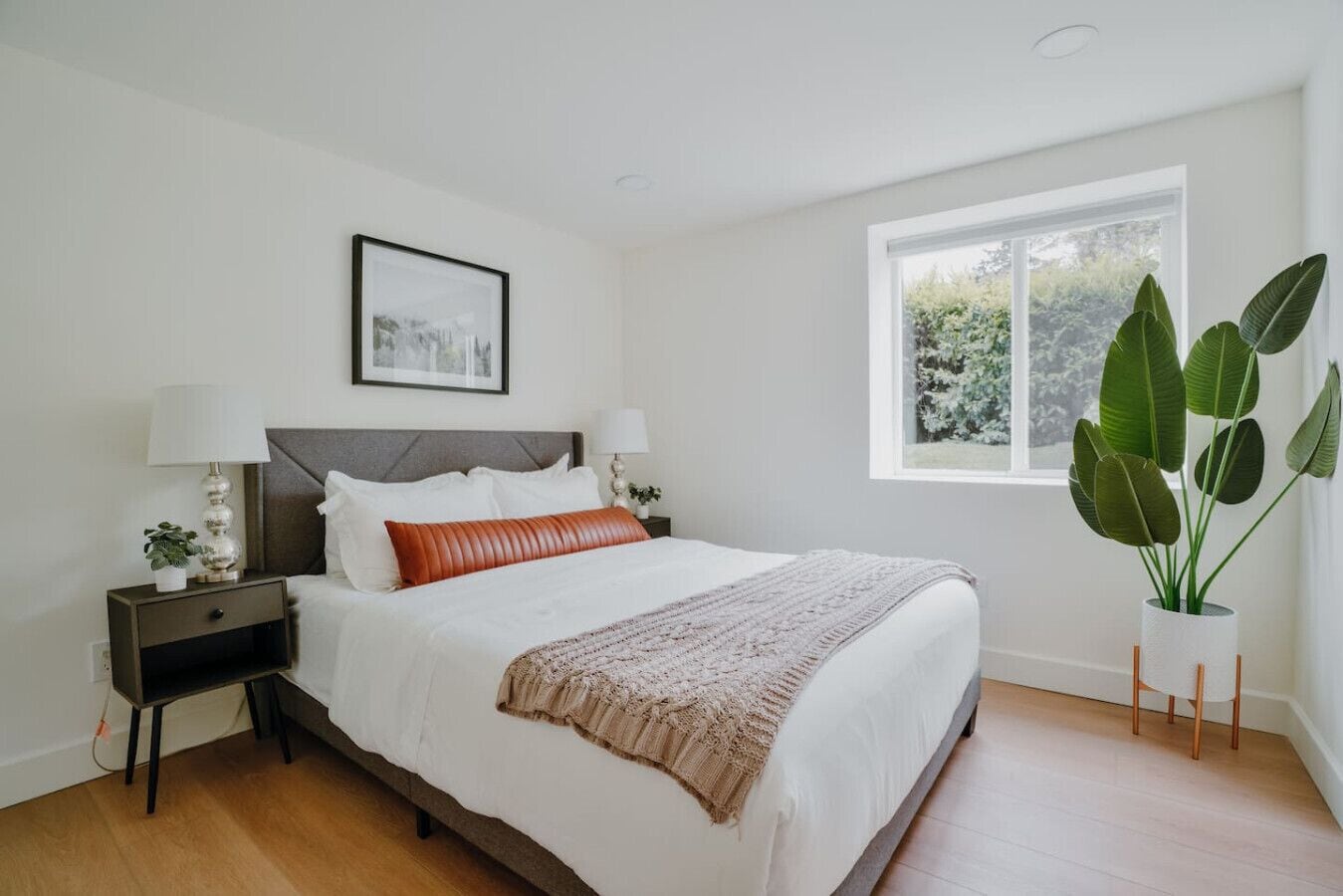 Un dormitorio moderno con una cama grande, dos mesitas de noche con lámparas, un cuadro enmarcado en la pared y una ventana con vistas a zonas verdes.