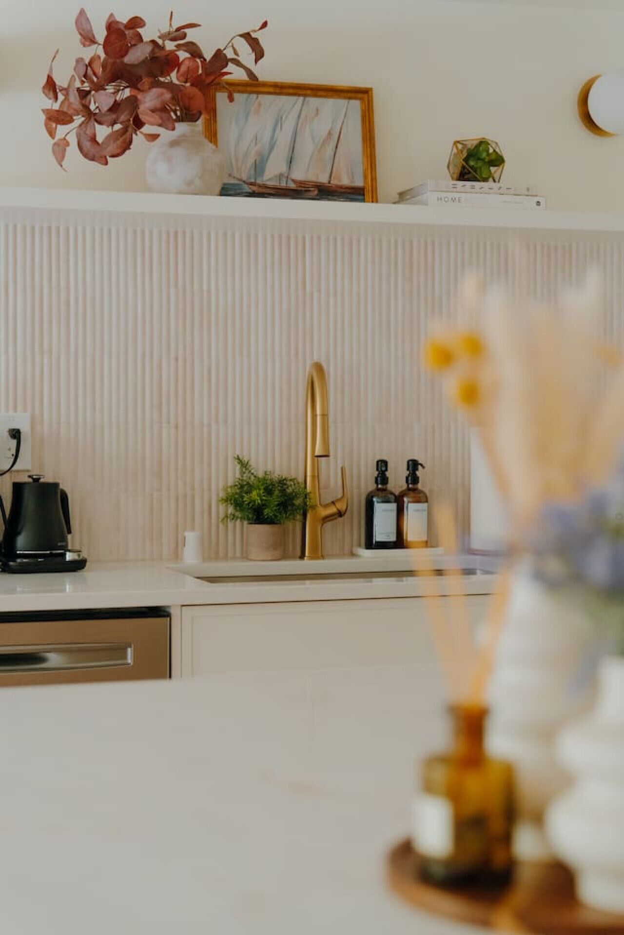 A kitchen with a modern design, featuring a white countertop, a gold faucet, and a potted plant.